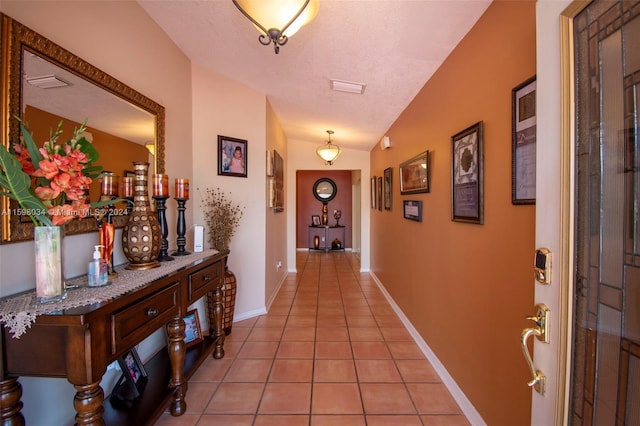 corridor with a textured ceiling, vaulted ceiling, and light tile patterned flooring