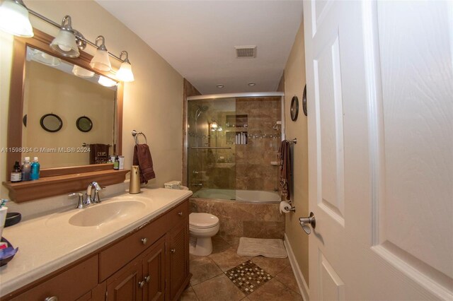 full bathroom with shower / bath combination with glass door, tile patterned flooring, vanity, and toilet