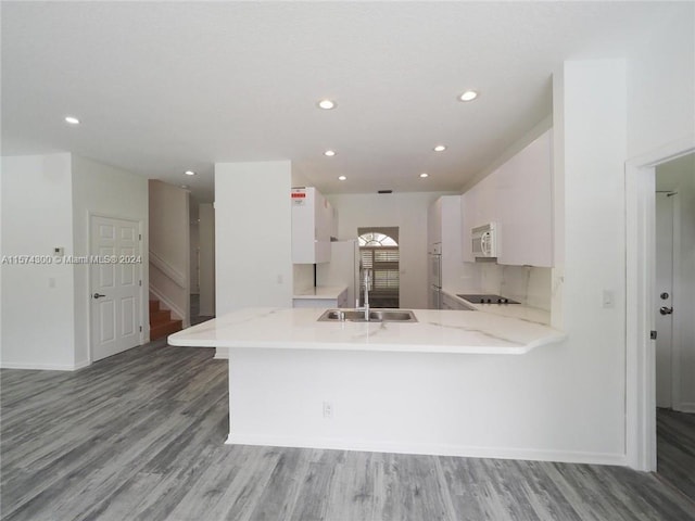 kitchen featuring white appliances, white cabinets, kitchen peninsula, hardwood / wood-style floors, and sink