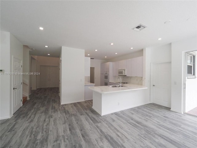 kitchen featuring white cabinets, sink, light wood-type flooring, and kitchen peninsula