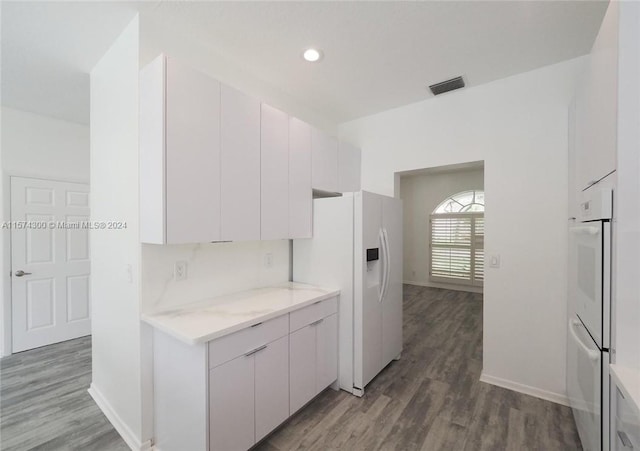 kitchen with wood-type flooring, white cabinets, light stone countertops, and white appliances