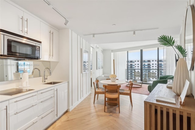 kitchen featuring light hardwood / wood-style flooring, rail lighting, white cabinetry, black appliances, and sink