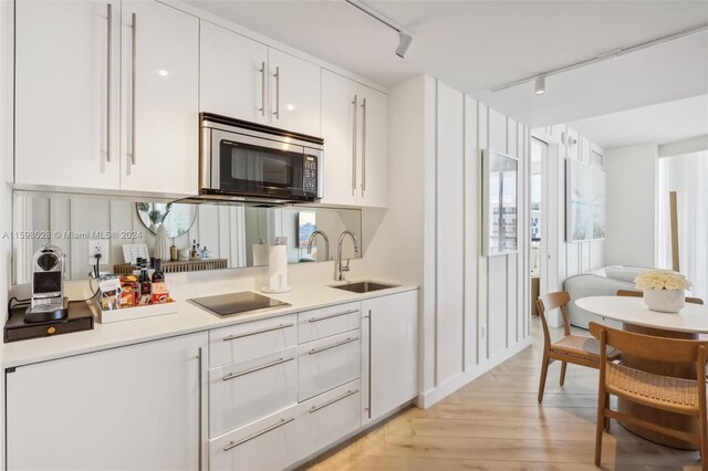 kitchen featuring white cabinetry, light wood-type flooring, black electric cooktop, sink, and track lighting