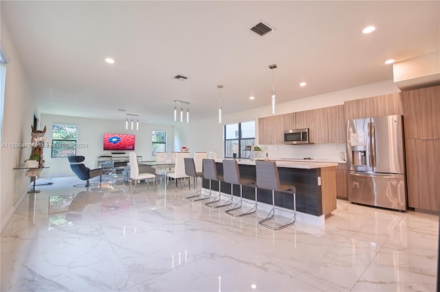 kitchen with appliances with stainless steel finishes, decorative light fixtures, a kitchen island with sink, and a healthy amount of sunlight