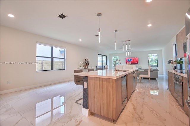 kitchen with a center island with sink, oven, hanging light fixtures, and plenty of natural light