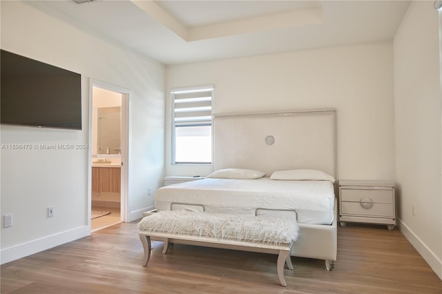 bedroom featuring a raised ceiling, hardwood / wood-style flooring, and ensuite bath