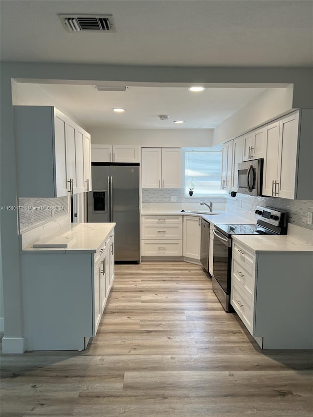 kitchen featuring light hardwood / wood-style flooring, tasteful backsplash, white cabinetry, appliances with stainless steel finishes, and sink