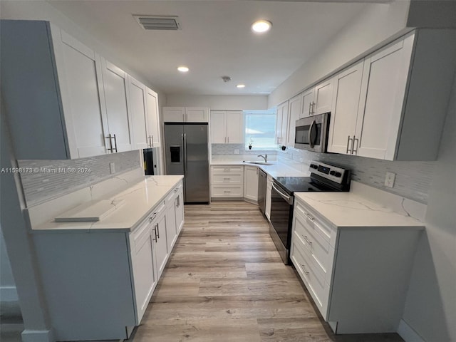 kitchen featuring stainless steel appliances, light stone countertops, white cabinets, and sink