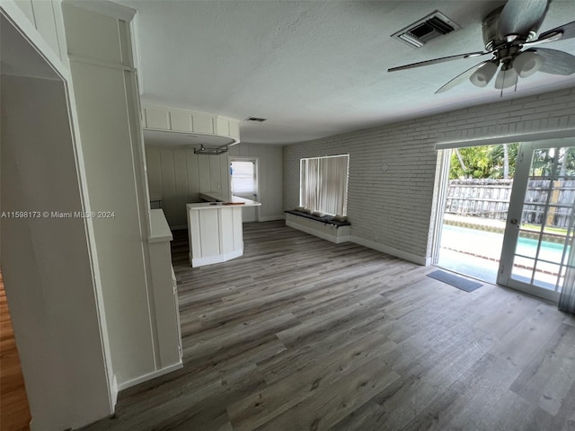 unfurnished living room featuring brick wall, ceiling fan, french doors, hardwood / wood-style flooring, and a textured ceiling