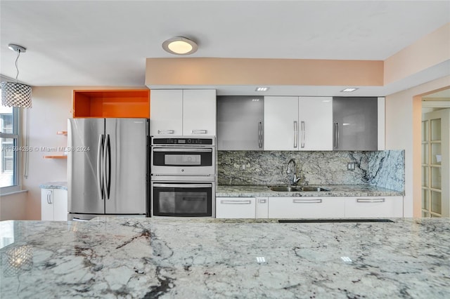 kitchen with decorative backsplash, light stone countertops, stainless steel appliances, sink, and white cabinets