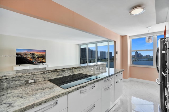 kitchen featuring pendant lighting, black electric stovetop, stainless steel fridge, light stone countertops, and white cabinetry