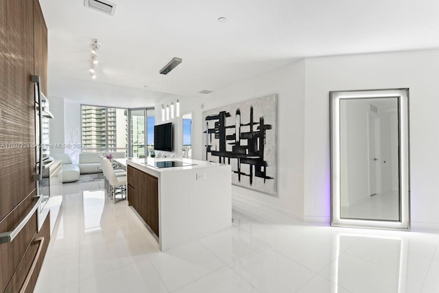 kitchen with black electric stovetop, an island with sink, light tile flooring, decorative light fixtures, and rail lighting