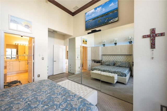 bedroom featuring a closet, ensuite bathroom, a towering ceiling, hardwood / wood-style flooring, and ornamental molding