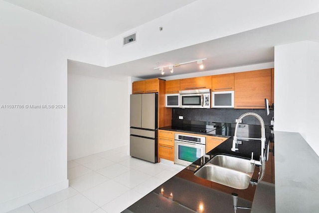 kitchen featuring a sink, appliances with stainless steel finishes, tasteful backsplash, brown cabinetry, and dark countertops