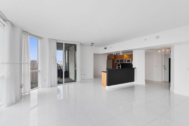 unfurnished living room with light tile patterned floors, baseboards, a chandelier, floor to ceiling windows, and a sink