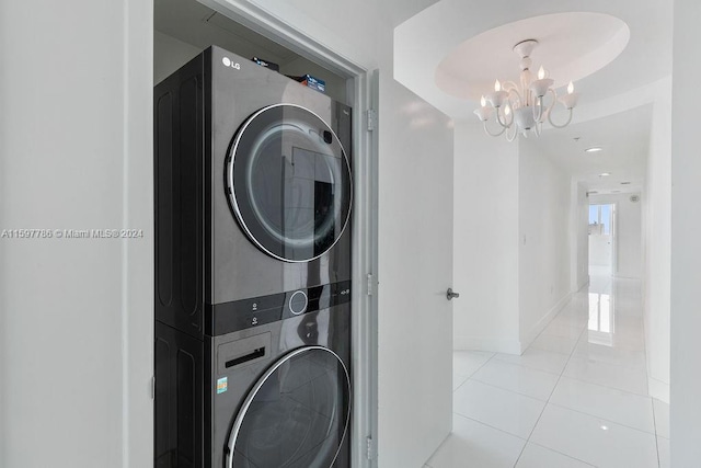 clothes washing area with stacked washer and dryer, light tile patterned floors, laundry area, baseboards, and a chandelier