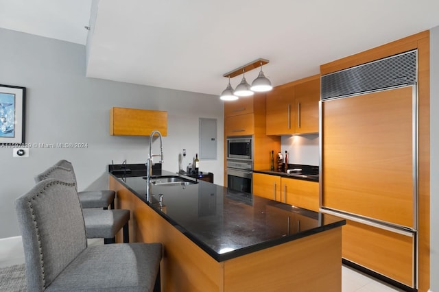 kitchen with hanging light fixtures, rail lighting, built in appliances, sink, and a breakfast bar