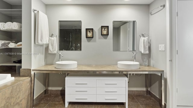 bathroom featuring a relaxing tiled bath, dual vanity, and tile floors