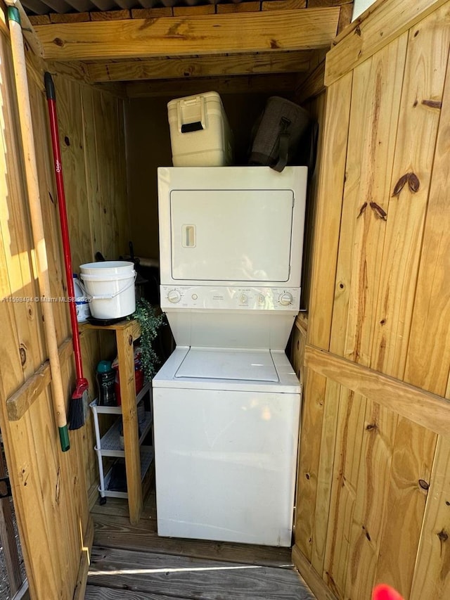 clothes washing area with wood walls, stacked washer / dryer, and wood finished floors