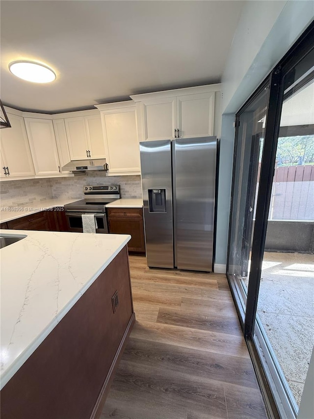 kitchen with light hardwood / wood-style flooring, white cabinetry, backsplash, stainless steel appliances, and light stone countertops