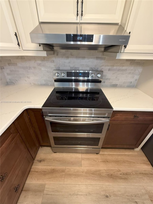 kitchen featuring stainless steel electric stove, range hood, backsplash, light stone countertops, and light hardwood / wood-style flooring