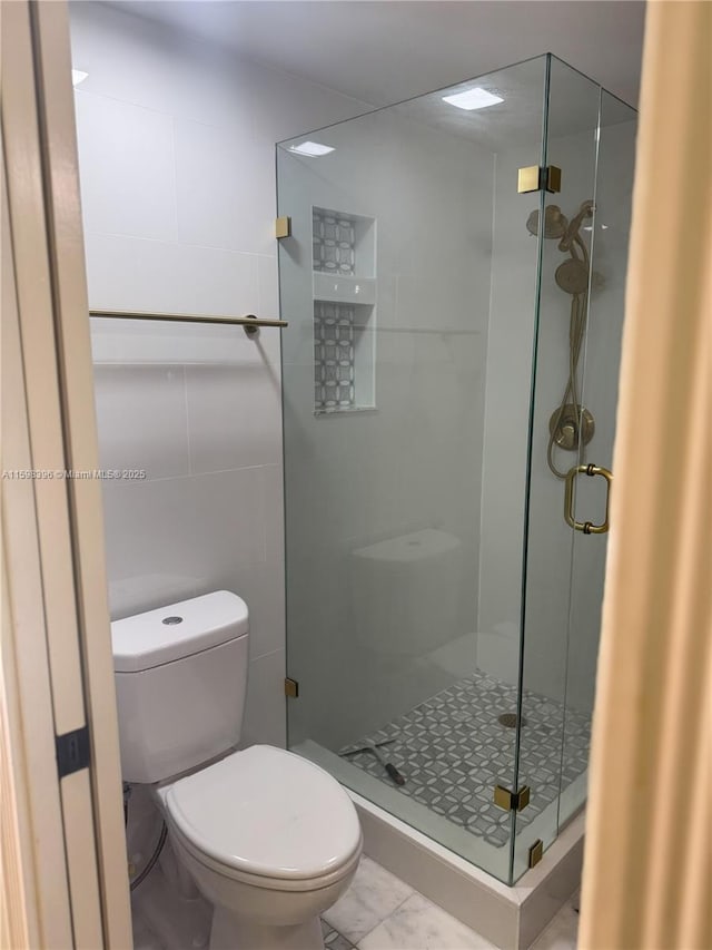 bathroom featuring toilet, a shower with shower door, and tile walls