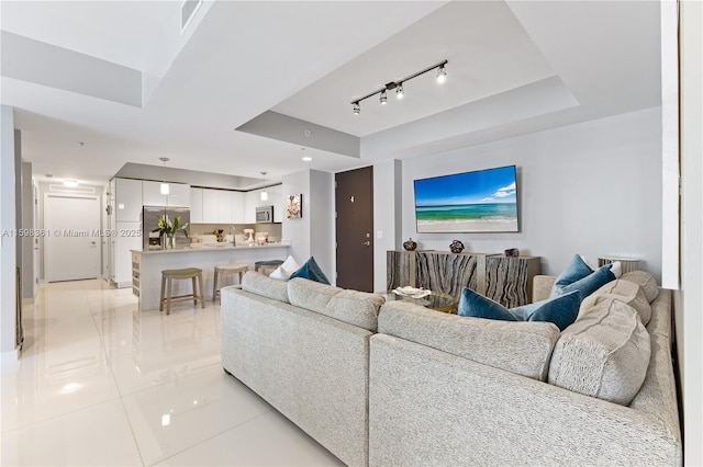 living room with light tile patterned floors, a raised ceiling, and sink