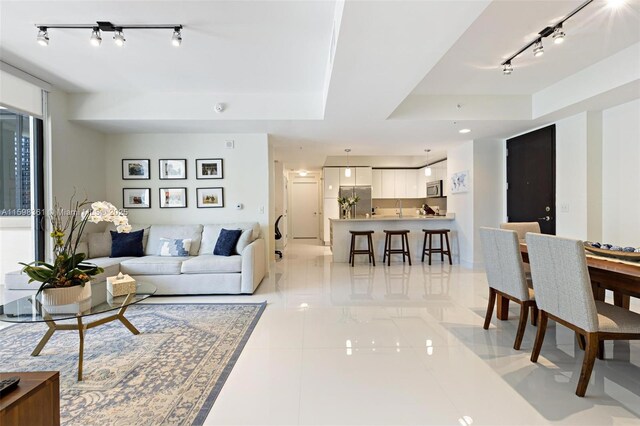 tiled living room featuring rail lighting and a raised ceiling