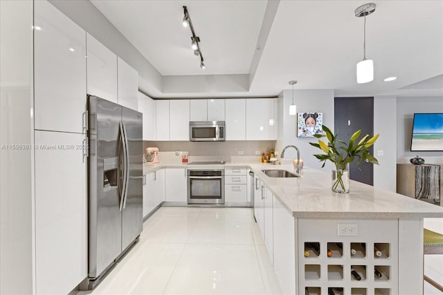 kitchen with appliances with stainless steel finishes, decorative light fixtures, track lighting, white cabinets, and sink