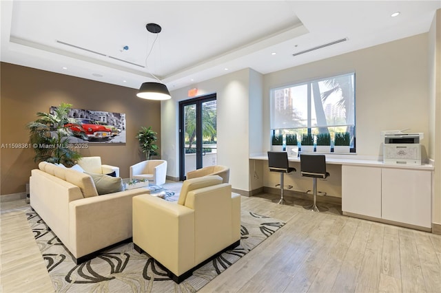 living room with light wood-type flooring, french doors, and a tray ceiling