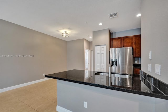 kitchen featuring kitchen peninsula, stainless steel fridge, light tile patterned floors, and dark stone countertops