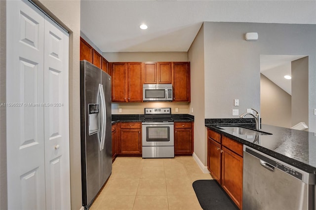 kitchen featuring kitchen peninsula, dark stone counters, stainless steel appliances, sink, and light tile patterned floors