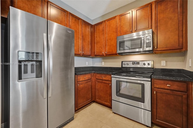 kitchen featuring light tile patterned floors, stainless steel appliances, and dark stone counters