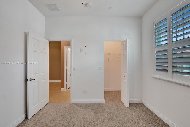 unfurnished bedroom featuring multiple windows, light carpet, a closet, and a spacious closet