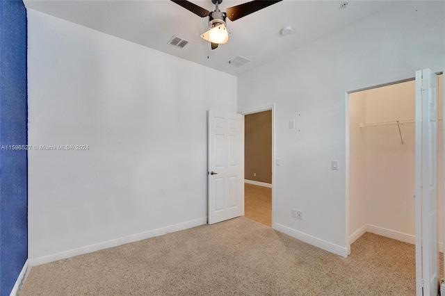 unfurnished bedroom with a high ceiling, a walk in closet, ceiling fan, light colored carpet, and a closet