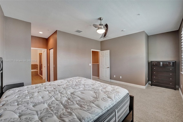 bedroom with ceiling fan, light carpet, and ensuite bath