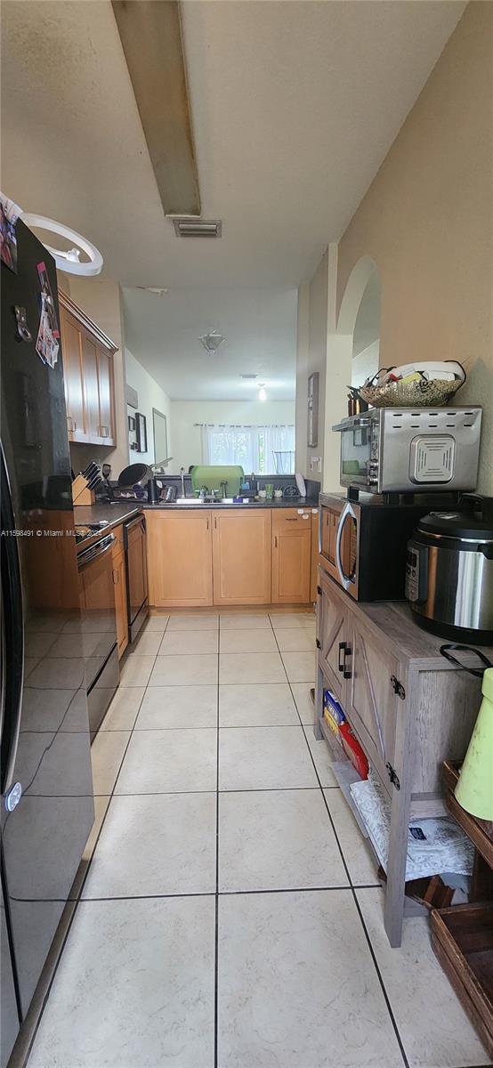 kitchen featuring black appliances, light tile patterned floors, and light brown cabinetry