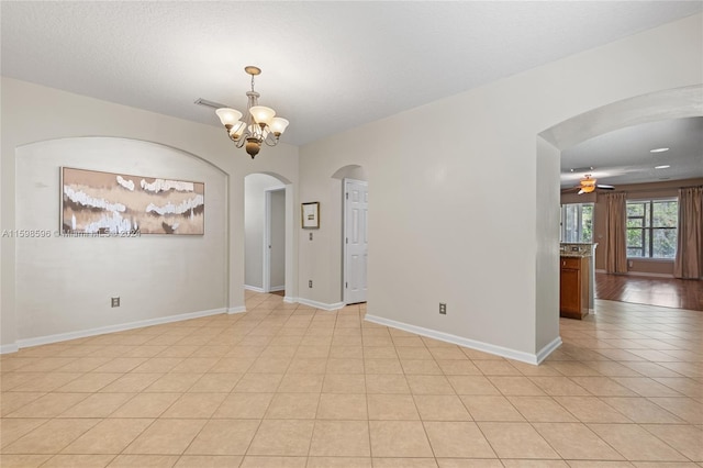 tiled empty room featuring ceiling fan with notable chandelier