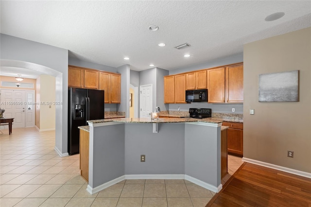 kitchen with black appliances, an island with sink, light wood-type flooring, light stone counters, and a textured ceiling