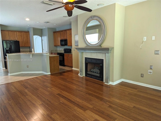 kitchen with black appliances, ceiling fan, a tile fireplace, kitchen peninsula, and dark tile patterned flooring