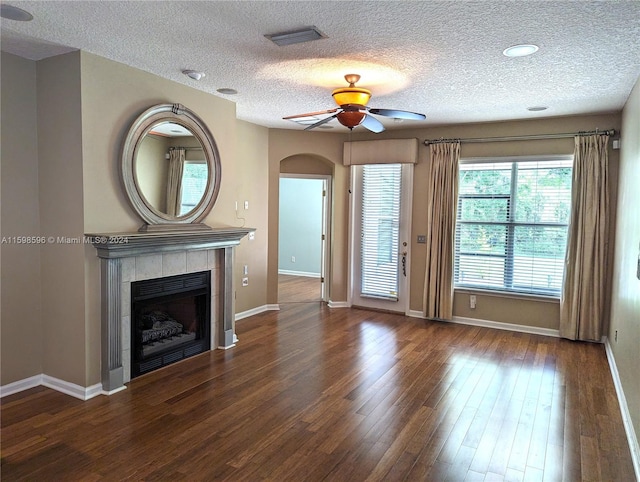 unfurnished living room featuring ceiling fan, dark wood-type flooring, a textured ceiling, and a tiled fireplace