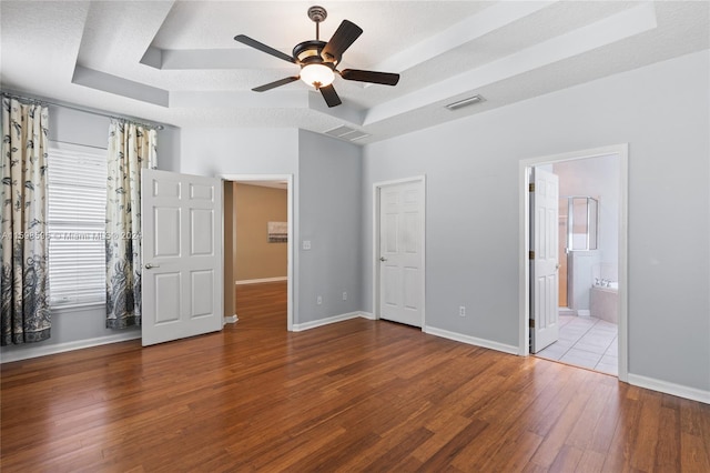 unfurnished bedroom with a textured ceiling, connected bathroom, ceiling fan, tile patterned floors, and a raised ceiling