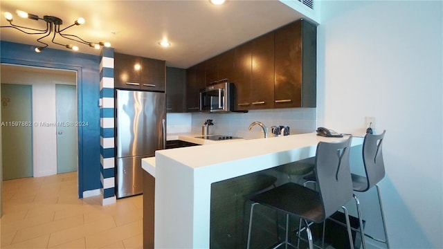 kitchen with appliances with stainless steel finishes, tasteful backsplash, a breakfast bar, and dark brown cabinetry