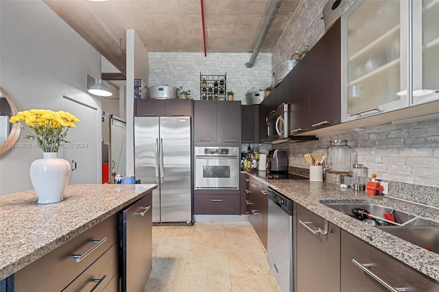 kitchen with light stone countertops, backsplash, dark brown cabinetry, stainless steel appliances, and sink