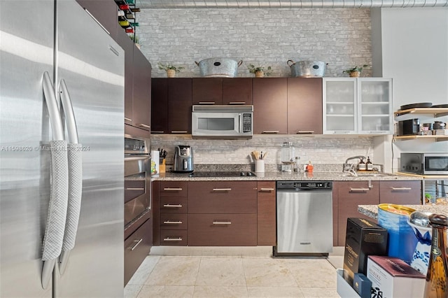 kitchen with sink, light stone counters, dark brown cabinets, light tile patterned flooring, and appliances with stainless steel finishes