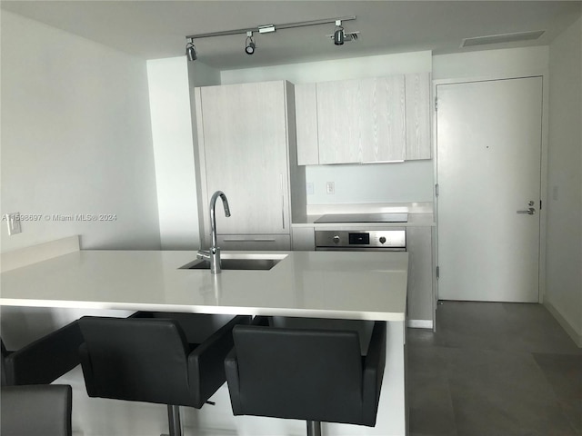 kitchen featuring a kitchen breakfast bar, rail lighting, stainless steel oven, sink, and stovetop