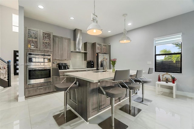 kitchen featuring pendant lighting, a breakfast bar, a center island with sink, sink, and wall chimney exhaust hood