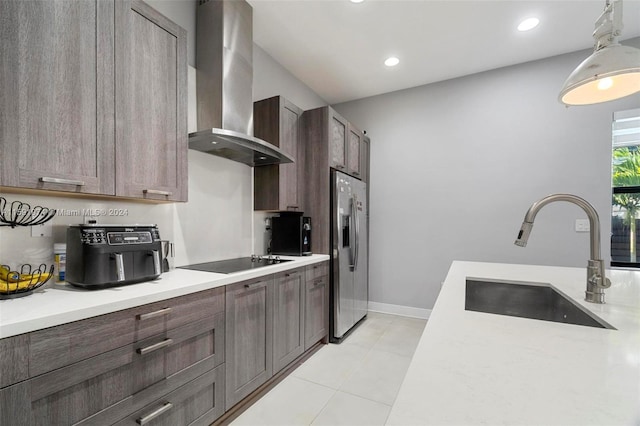 kitchen featuring sink, hanging light fixtures, wall chimney exhaust hood, stainless steel fridge, and black electric cooktop