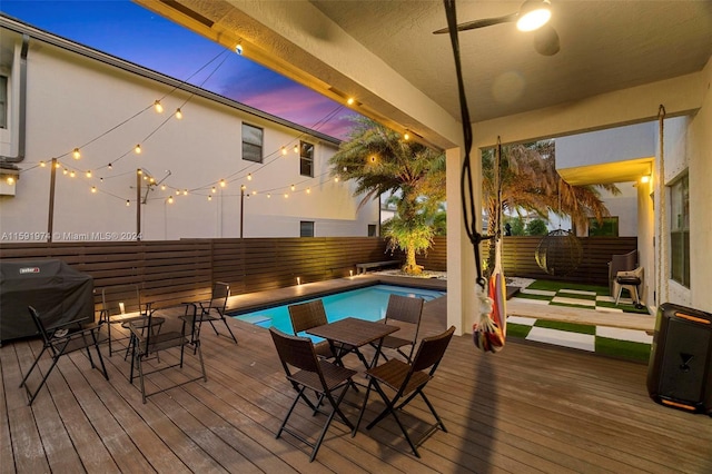 pool at dusk featuring a grill and a deck