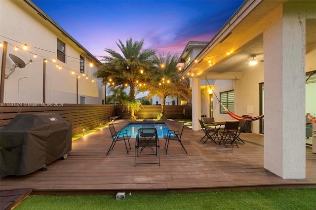 deck at dusk with a fenced in pool and grilling area